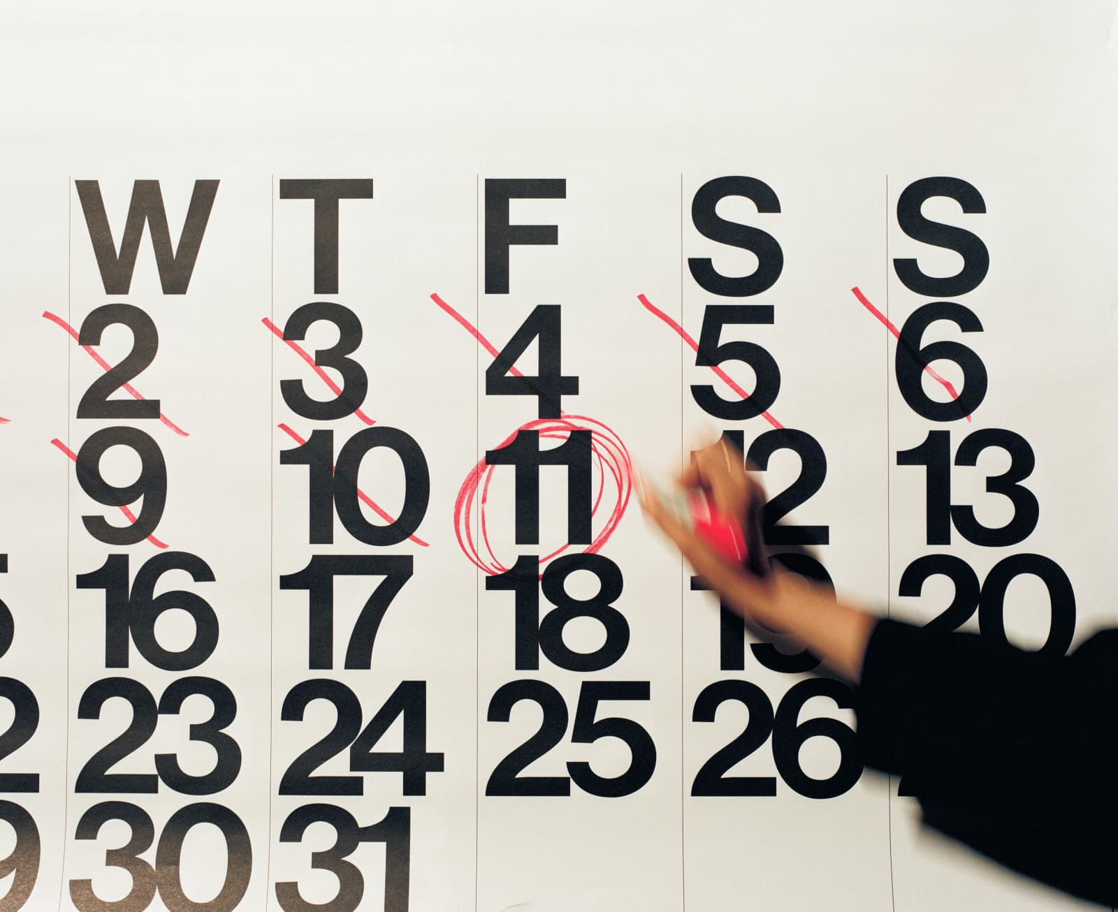 Hand kreist mit rotem Marker die 11 auf einem großen Wandkalender ein, die Tage davor sind durchgestrichen